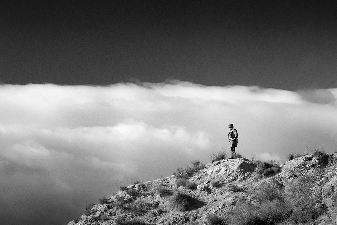A lone service member on a hill beneath clouds.